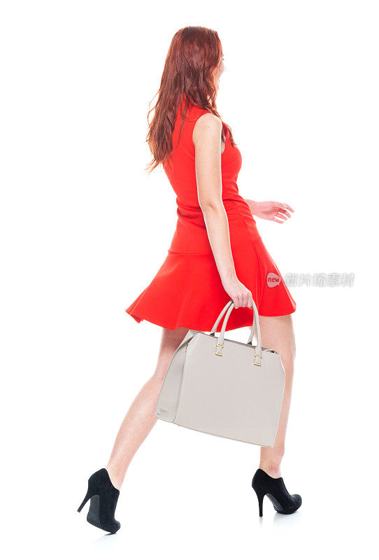 完整的长度/一个人/ 18-19岁美丽的红发白人年轻女性的后视图十几岁的女孩走穿着裙子和高跟鞋，拿着钱包
